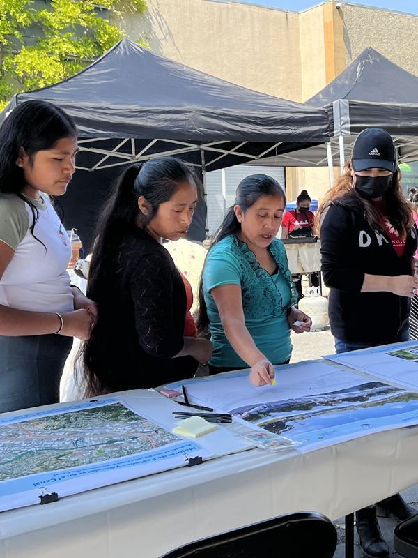 Planning in Spanish - post - apr2025 Four women visit table at an in-person community event