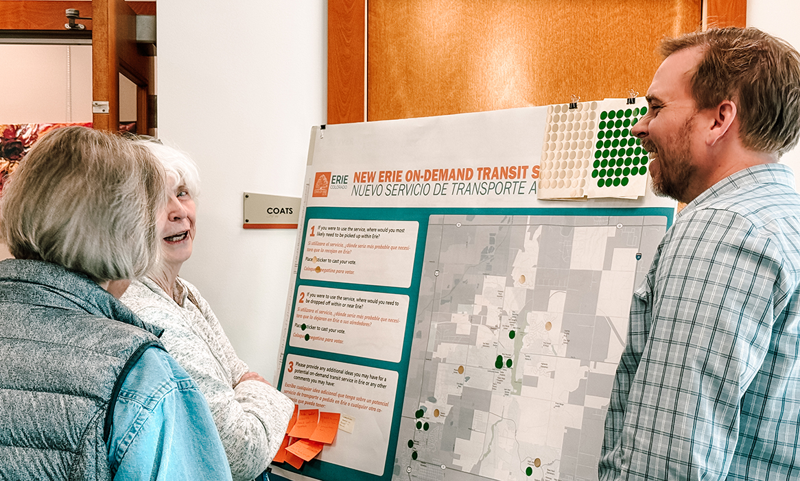 Erie Outreach - Page - Jan2025 Group of people converse around an outreach poster at an event in Erie Colorado