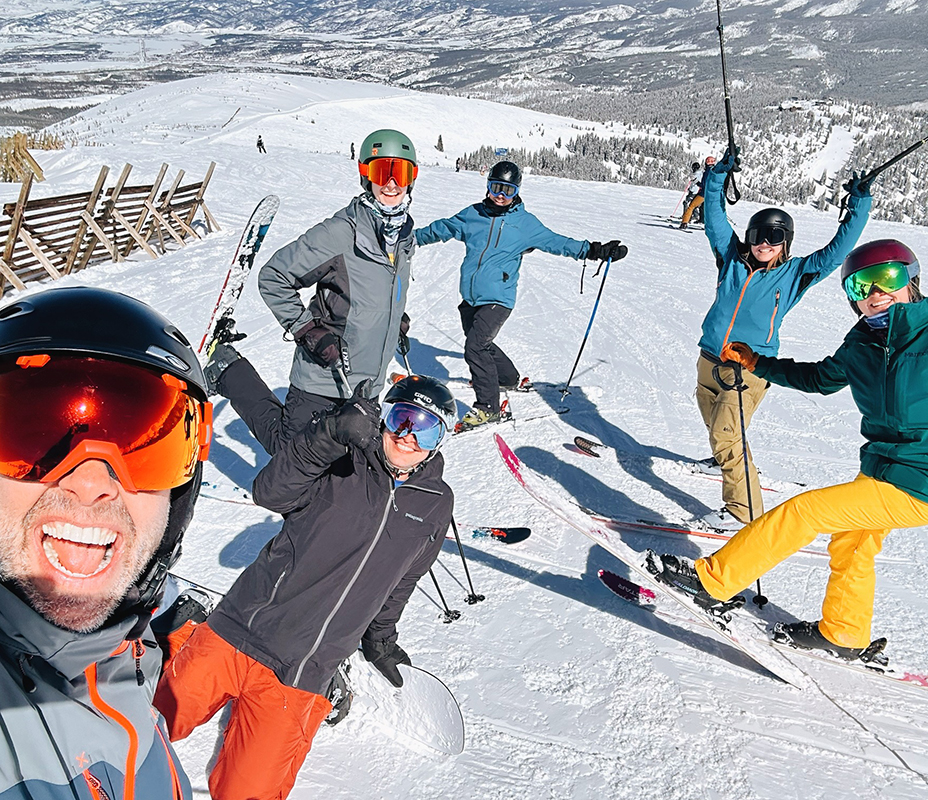 Ski trip - Page - Jan2025 Six people pose excitedly during a ski trip at the top of a snow covered ski run