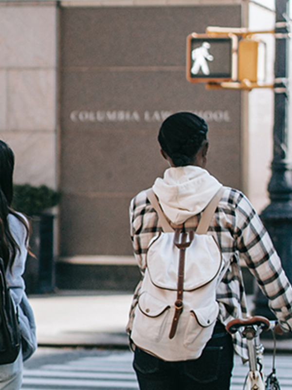 Two young women walk their bicycles across a crosswalk