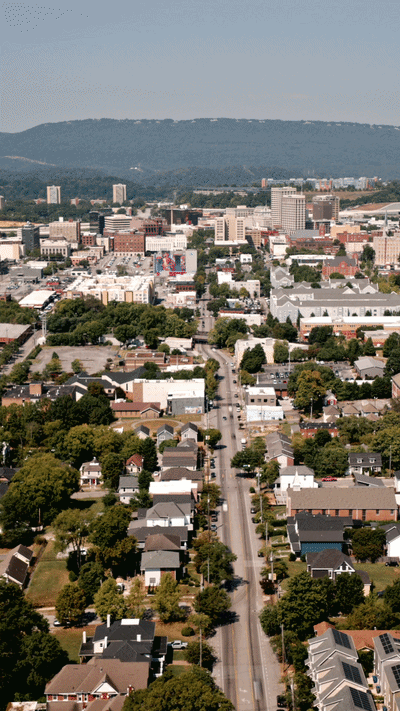 Aerial video showing cars and people moving through a long corridor with residential, urban and rural areas.