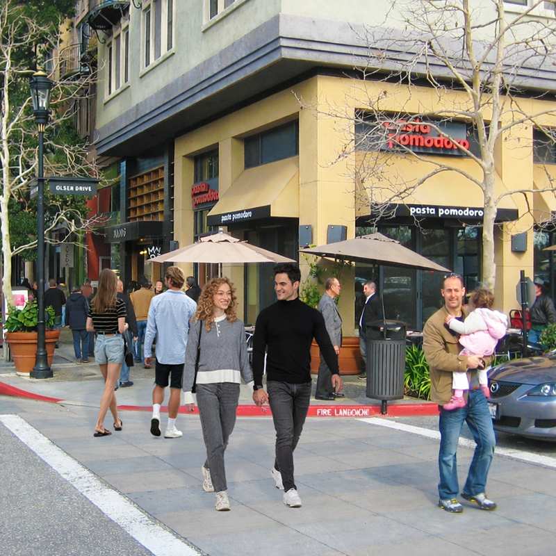 Pedestrians walking in front of a mixed-use building - showing both shopping on the lower levels and residential units on the top levels.