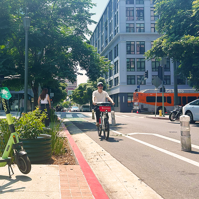 Man on a bike riding down a bike lane while a woman walks on the sidewalk in the city.